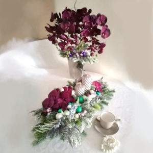 Fioletowy stroik na stół W tym uroczym Świątecznym stroiku wykorzystane materiały to między innymi ośnieżone gałązki, duże storczyki w przepieknym kolorze bakłażana, szklane szklane oraz dwie piękne srebrno-szare świece na drewnianej podstawie. Wszystkie kwiaty wykorzystane bukiecie to wysokiej jakości sztuczne kwiaty. Jest to elegancka alternatywa dla osób chcących w piękny sposób przyozdobic swój dom. Co więcej, do tej kompozycji możemy przygotować również inne elementy dekoracyjne, takie jak wieńce, stroiki, bukiety itp., zgodnie z Waszymi życzeniami, które możecie nam przekazać telefonicznie lub mailowo. Wymiary kompozycji Długość 70 cm Szerokość 34 cm, Zestaw świąteczny fioletowe bogactwo