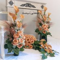 Zestaw nagrobny w Cieniu Kasztanowca nr 380 Zestaw nagrobny w Cieniu Kasztanowca nr 380 to unikatowa i piękna kompozycja kwiatowa. Zestaw składa się z kompozycji leżącej oraz bukietu.  Kompozycja jest przede wszystkim jest niezwykle elegancka i duża. Składają się na nią kolejno : róże i gumowe kalie .10 kalii w kolorze cappuccino o długości 72 cm  zostało ułożone warstwowo w kuli kwiatowej. Całość osadzona jest na betonowej podstawce, by zabezpieczyć kompozycję przed wiatrem. Kalie i róże pięknie ze sobą współgrają tworząc harmonijną całość. Bukiety stworzone do zestawu będą strzeliste , w kolorze naturalna biel, z pięknymi powyginanymi kaliami. Możliwość zamówienia w następującej kolorystyce: czerwony, biały, fioletowy, bordo, różowo-kremowy, szary, szaro-różowy, szaro-fioletowy, szaro-niebieski. Wiązanka będzie prezentować się elegancko na praktycznie każdym większym nagrobku. Wszystkie kwiaty wykorzystane w kompozycji to wysokiej jakości sztuczne kwiaty. Jeżeli spodobała się Wam nasza Kompozycja nagrobna Zestaw nagrobny w Cieniu Kasztanowca nr 380,  możemy również przygotować dla Państwa zestaw w tej kolorystyce, z innymi elementami dekoracyjnymi, na przykład z bukietem do wazonu, stroikiem czy wiankiem. Wystarczy napisać do nas wiadomośc prywatną, by ustalić szczegóły zamówienia Wymiary Zestawu nagrobnego w Cieniu Kasztanowca nr 380: Długość  85-90 cm Wysokość bukietów: ok. 75-80 cm Nie ma dwóch takich samych Każda z naszych dekoracji jest wykonywana ręcznie, więc gwarantujemy, że dekoracja dostarczona Wam będzie jedyna w swoim rodzaju. Ze względu na to, że nasze kompozycje wykonywane są za każdym razem ręcznie przez florystę oraz sezonowość wykorzystywanych w kompozycjach dodatków – kompozycja przygotowana dla Państwa może delikatnie różnić się od przedstawionej na zdjęciu. Gwarantujemy natomiast jakość i estetykę wykonania Państwa zamówienia.